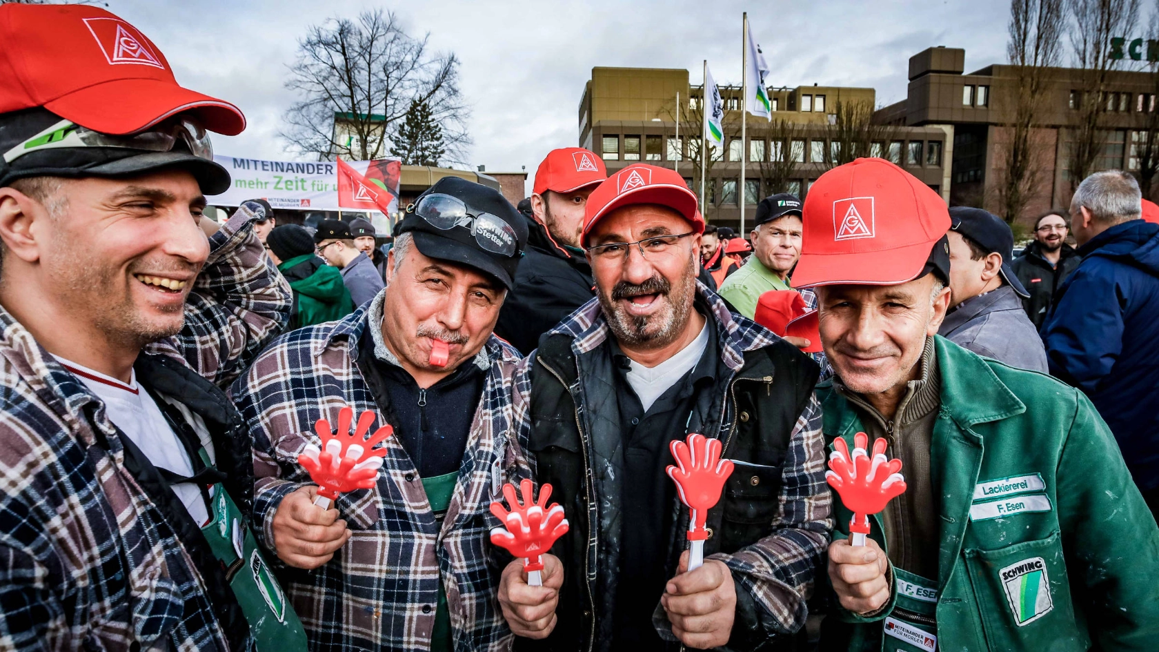 Lachende Männer in Arbeitskleidung und IG Metall-Kappen.